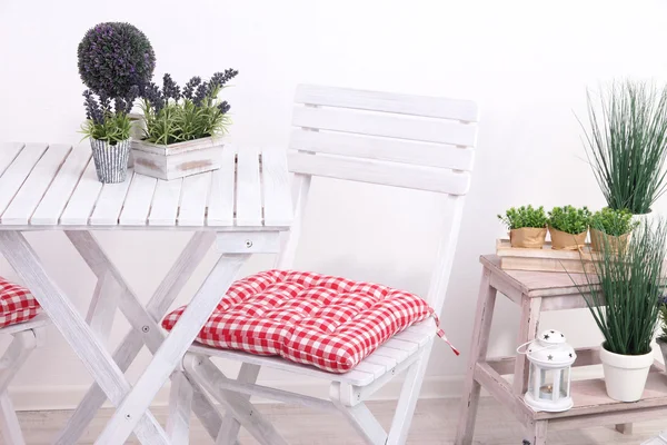 Garden chair and table with flowers on wooden stand on white background