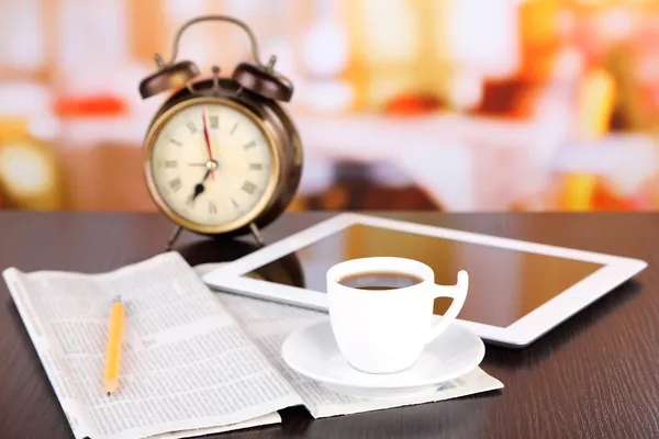 Tablet, newspaper, cup of coffee and alarm clock on wooden table