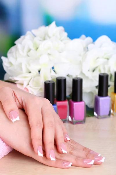 Beautiful woman hands with french manicure and flower on bright background