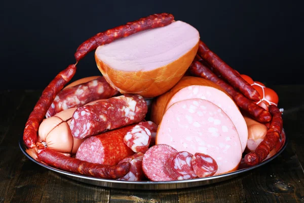 Lot of different sausages on salver on wooden table on black background