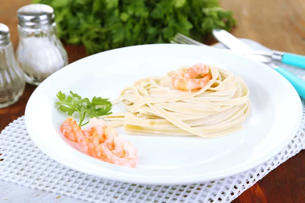 Pasta with shrimps on white plate, on wooden background