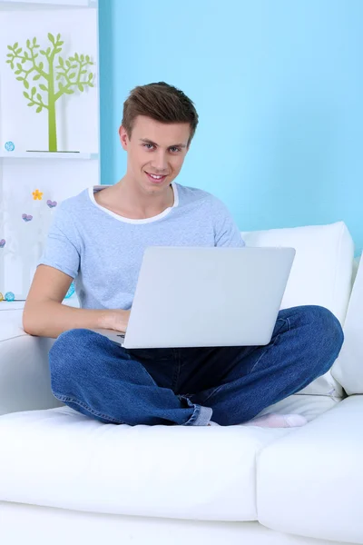 Guy sitting on sofa with laptop on blue background