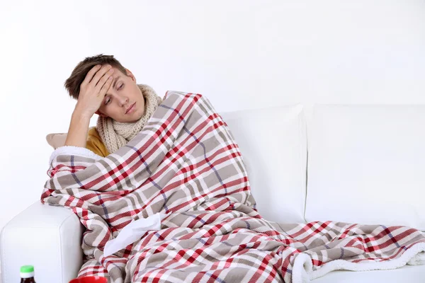 Guy wrapped in plaid sitting on sofa is ill
