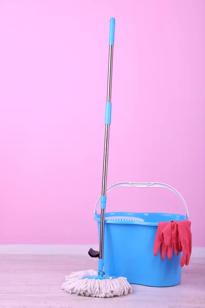 Floor mop and bucket for washing in room on pink wall background