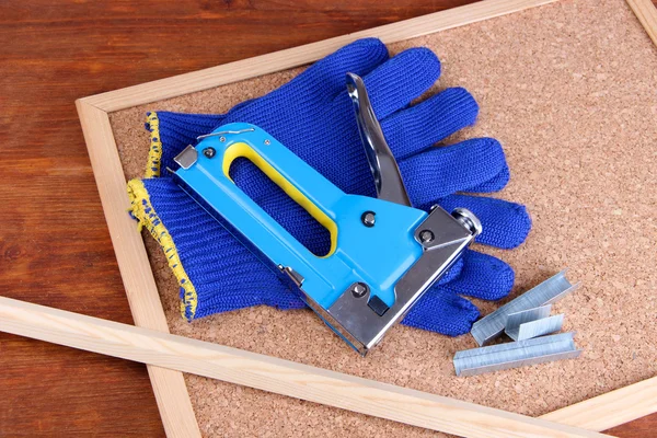 Construction stapler with gloves and staples on cork board close up