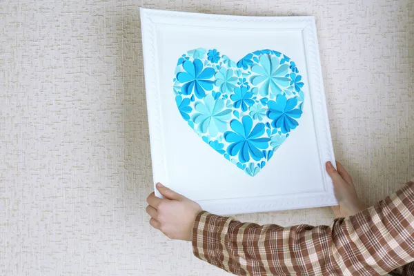 Woman hanging up picture with heart from paper flowers