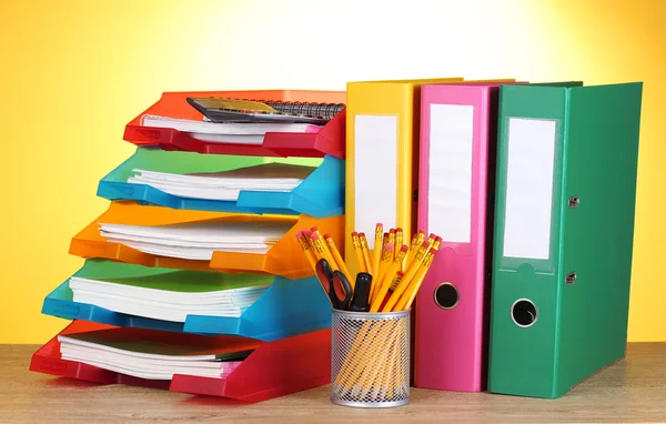 Bright paper trays and stationery on wooden table on yellow background