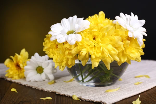 Beautiful chrysanthemum flowers in vase on table on dark yellow background