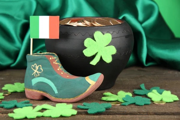 Saint Patrick day boot, pot of gold coins and clover leaves on green satin background