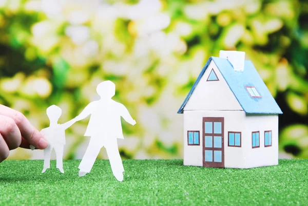 Little house and paper people on green grass, on bright background