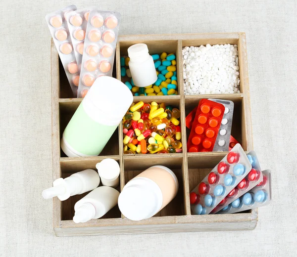 Medical pills, ampules in wooden box, on color background