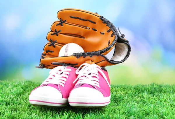 Beautiful gumshoes and baseball ball, glove on green grass, on bright background