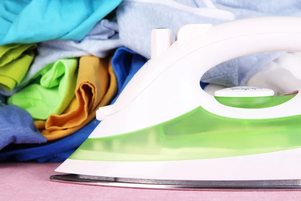 Iron and pile of colorful clothes  on table close up