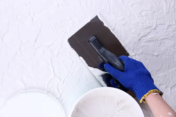 Construction trowel and worker hands on wall with textured plaster
