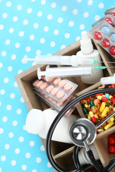 Medical pills,stethoscope, ampules in wooden box, on color background