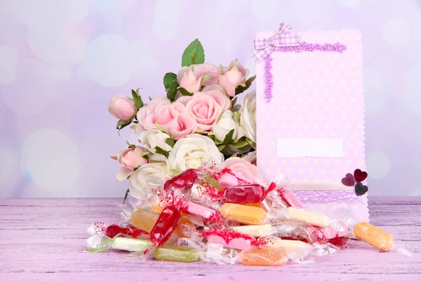 Tasty candies with flowers and card on table on bright background