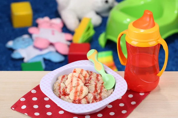Bowl of porridge for baby and toys  on table, on toys background