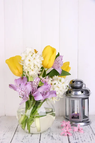 Flowers in vase with decorative lantern on table on wooden background
