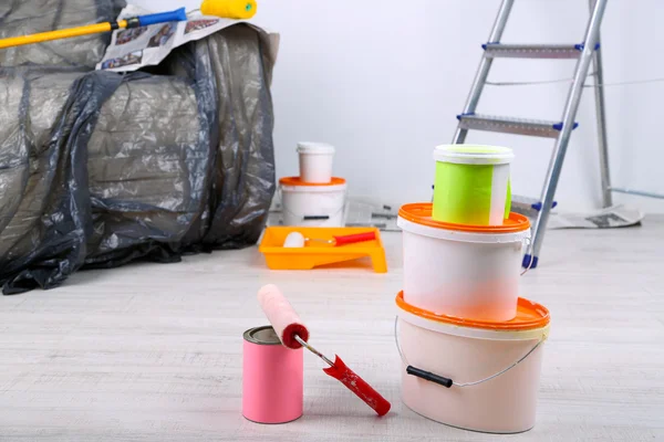 Buckets with paint, wrapped sofa and ladder on wall background. Conceptual photo of repairing works in room