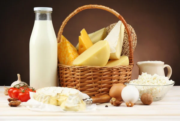 Basket with tasty dairy products on wooden table, on dark brown background