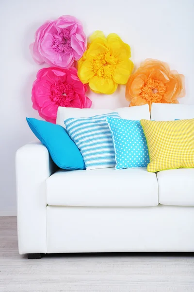 White sofa with colorful pillows in room on bright wall background