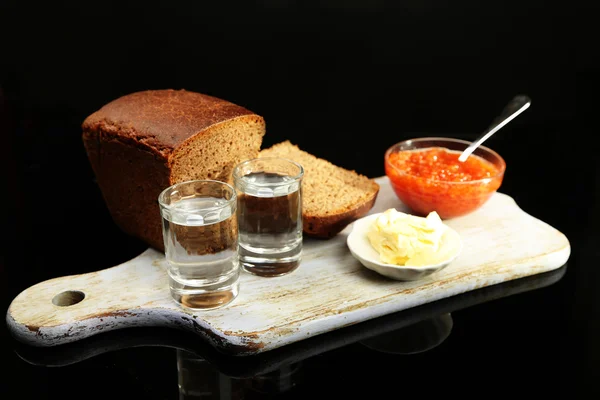 Composition with glasses of vodka, red caviar, fresh bread on wooden board,  isolated on black