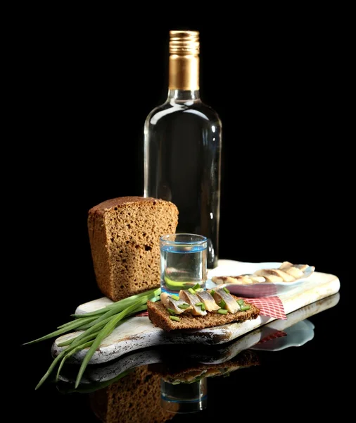 Composition with bottle of vodka, sandwich with salted fish, green onion and glass on wooden board, isolated on black