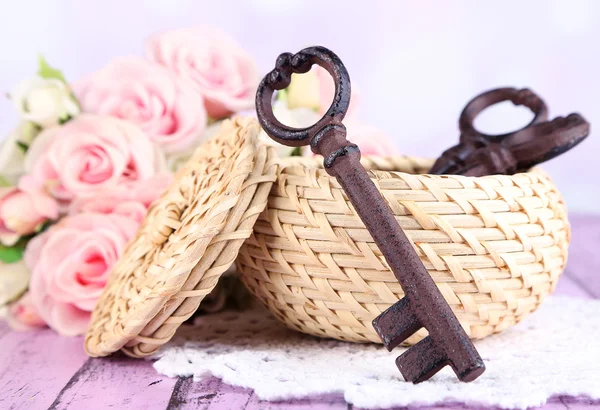 Key to success and happiness. Composition with keys in wicker basket and flowers. Conceptual photo. On color wooden table, on light background