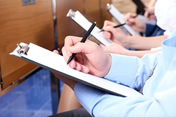 Hands holding pens and making notes at conference