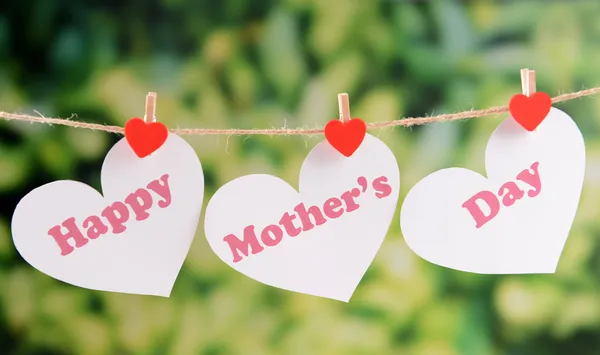 Happy Mothers Day message written on paper hearts with flowers on bright background
