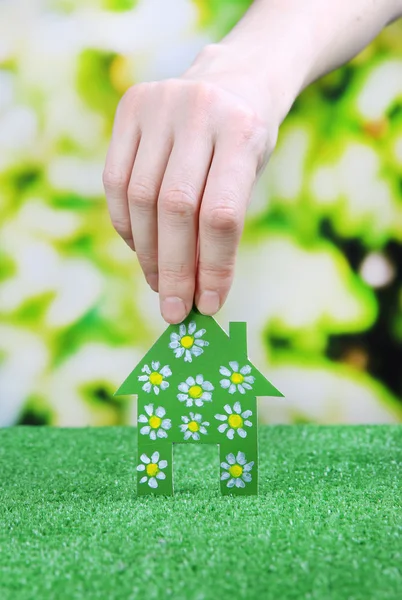 Little paper house in hand on green grass on bright background