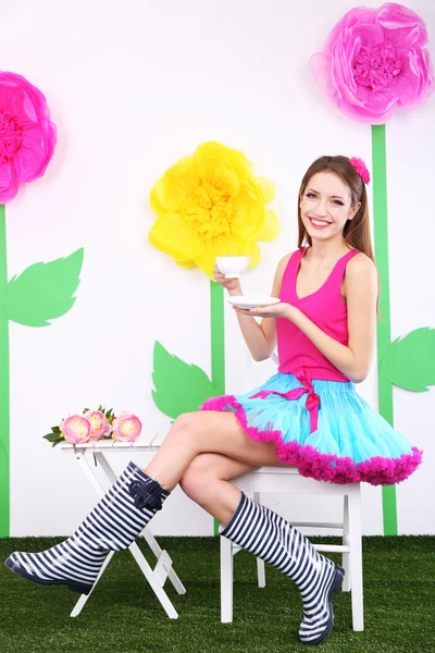 Beautiful young woman in petty skirt sitting on chair on decorative background