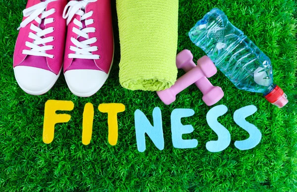 Fitness and healthy life. Conceptual photo. Gumshoes, towel, dumbbells and water bottle on green grass background