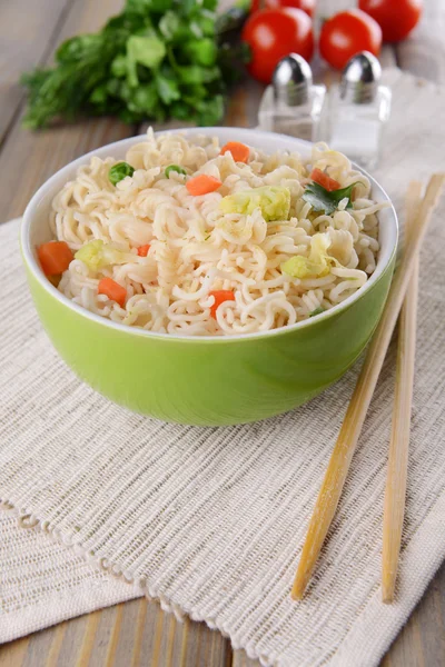 Tasty instant noodles with vegetables in bowl on table close-up