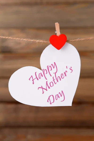 Happy Mothers Day message written on paper heart on brown background