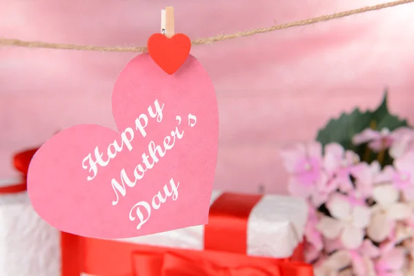Happy Mothers Day message written on paper heart with flowers on pink background
