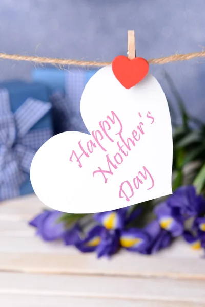 Happy Mothers Day message written on paper heart with flowers on purple background