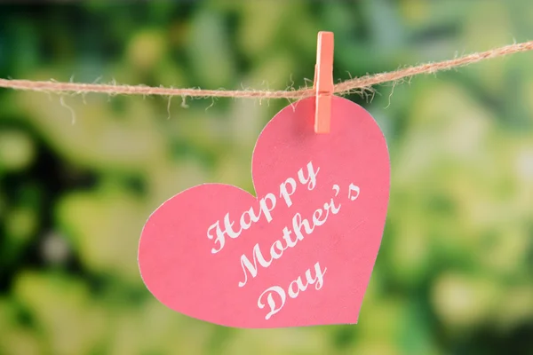 Happy Mothers Day message written on paper heart with flowers on bright background
