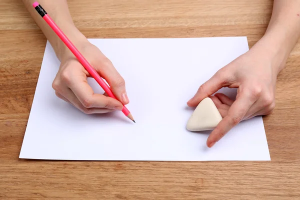 Human hands with pencil writing on paper and erase rubber on wooden table background