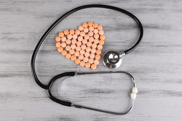 Heart of pills and stethoscope on wooden background