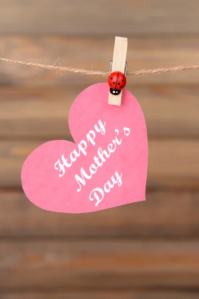 Happy Mothers Day message written on paper heart on brown background