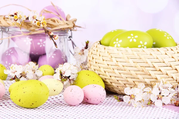 Composition with Easter eggs in glass jar and wicker basket, and blooming branches on light background