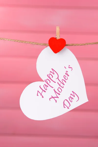 Happy Mothers Day message written on paper heart on pink background