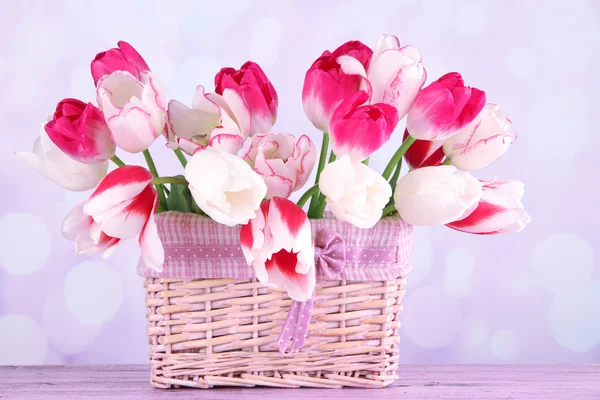 Beautiful tulips in wicker basket, on light background
