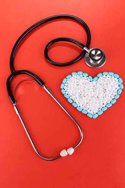 Heart of pills and stethoscope on red background