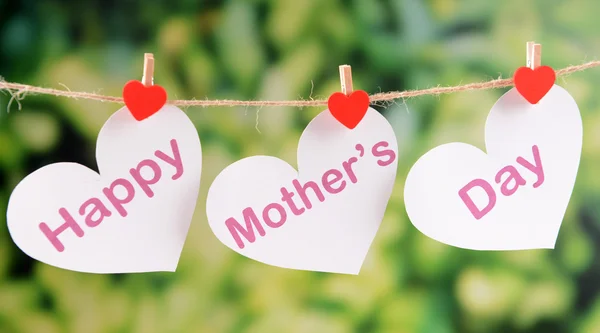 Happy Mothers Day message written on paper hearts with flowers on bright background