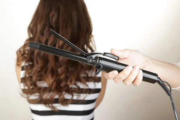 Stylist using curling iron for hair curls, close-up, isolated on white