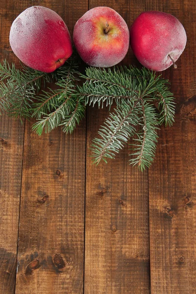 Red frosted apples with fir branch on wooden background