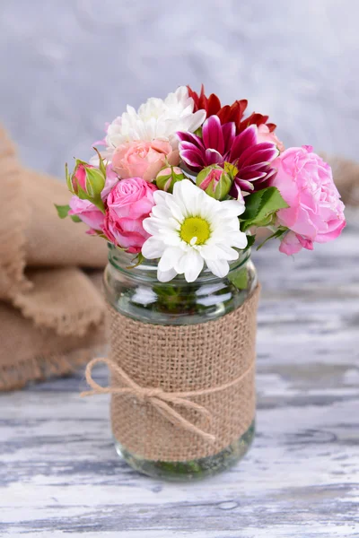Beautiful bouquet of bright flowers in jar on table on grey background