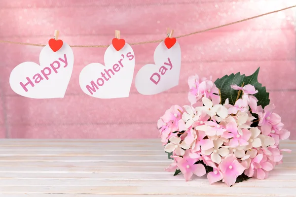 Happy Mothers Day message written on paper hearts with flowers on pink background